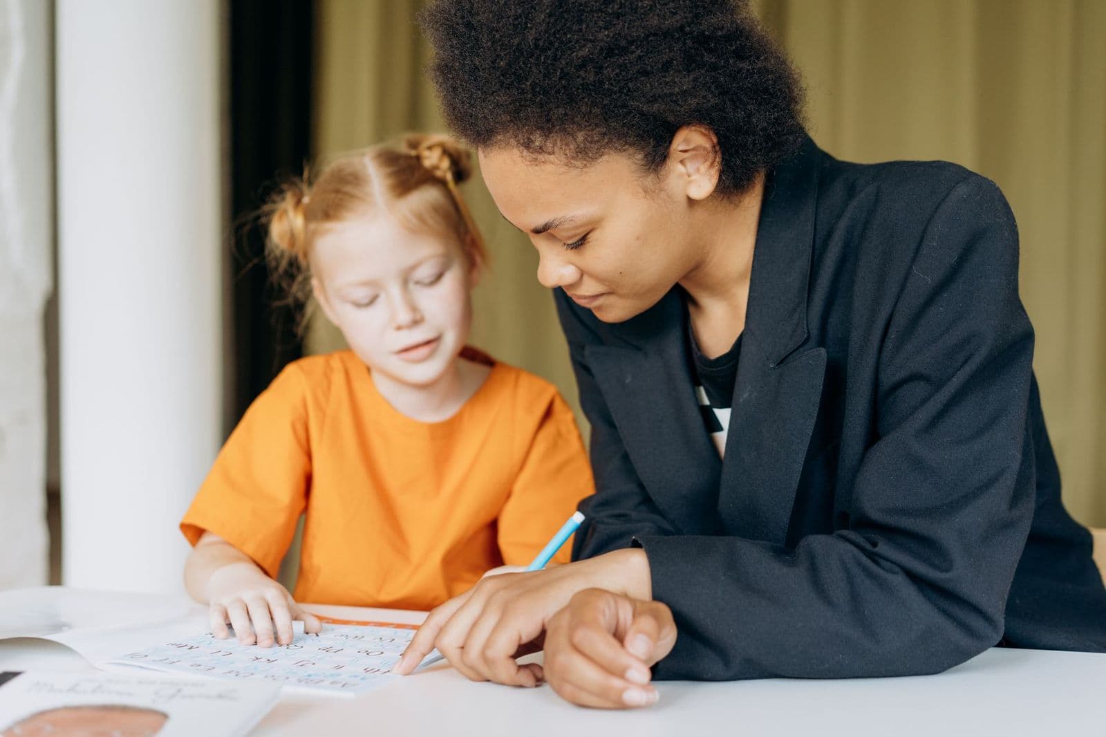 A tutor helping a young student with her writing at a desk