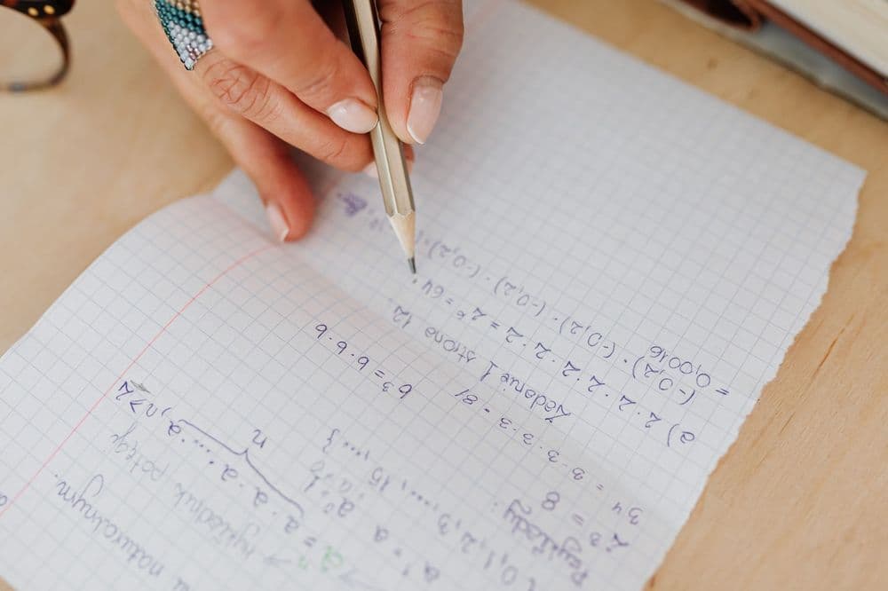 Maths equations handwritten in pencil on squared paper